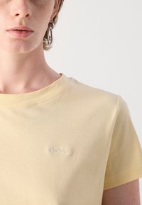 T-shirt giallo a maniche corte realizzato in morbido cotone, caratterizzato da un piccolo logo "BOSS" ricamato sul petto. Texture liscia e design semplice.