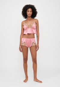 Roze satijnen lingerie set bestaande uit een v-hals cami met kantaccenten en bijpassende shorts met kantdetails. Zachte textuur en een ontspannen pasvorm.