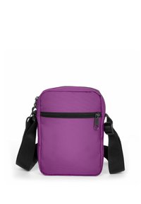 Sac bandoulière en nylon violet avec un compartiment principal zippé, une poche zippée à l'avant et une sangle noire réglable. Texture lisse, forme rectangulaire.