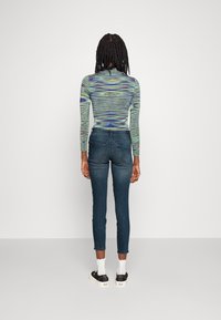 Camiseta de manga larga ajustada con un patrón de olas multicolor en verde y azul, combinada con unos jeans skinny oscuros y zapatillas de plataforma negras.
