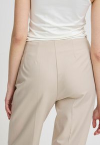 Beige kalhoty s přiléhavým střihem, vyrobené z hladkého materiálu, s centrálními sklady a vysokým pasem, spárované se jednoduchým bílým topem.