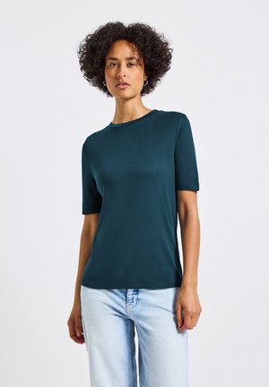Teal t-shirt met korte mouwen, gemaakt van een zachte, ademende stof. Ronde halslijn en een relaxte pasvorm. Gekocht met lichtblauwe jeans.