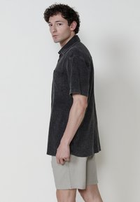Camisa de manga corta en tejido texturizado gris oscuro, con cuello abotonado y un bolsillo en el pecho, combinada con pantalones cortos beige claro.