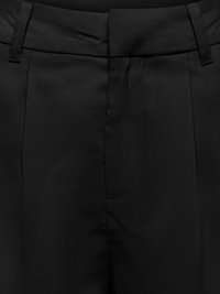 Gros plan sur un tissu noir montrant une ceinture cintrée, des passants de ceinture et des détails des coutures avant d'un pantalon formel.