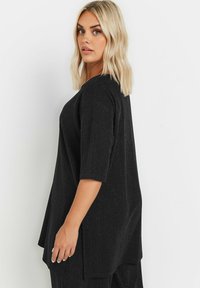 Tunic nera con una vestibilità rilassata, caratterizzata da un delicato motivo testurizzato, maniche 3/4 e spacchi laterali per facilitare i movimenti.