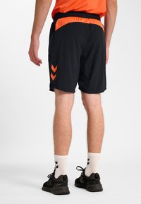 Svarta sportshorts med orange accenter och chevrondetaljer, tillverkade i lätt material. Har resår i midjan för komfort.