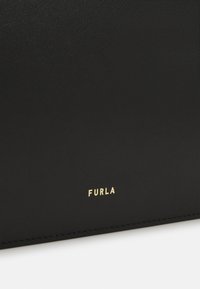 Melnas ādas soma ar teksturētu virsmu, uz kuras priekšpusē ir zelta iespiests logo "Furla". Šuvju detaļas apkārt malām.