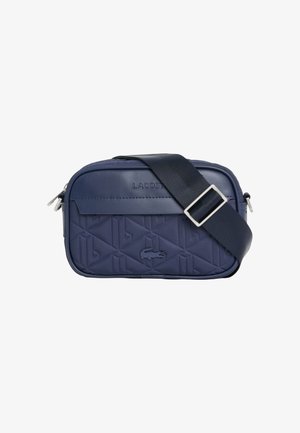 Bolso bandolera rectangular azul marino con correa negra ajustable, patrón geométrico en relieve, logo de Lacoste y compartimentos con cremallera.