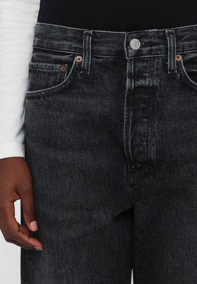 Pantalones vaqueros de denim negro con corte recto, que cuentan con un botón y remaches en tono cobre, diseño de cinco bolsillos y un acabado texturizado sutil.