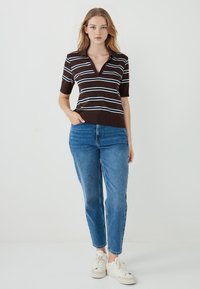 Bruin gestreept polo-shirt met korte mouwen, met witte en lichtblauwe lijnen, gecombineerd met blauwe spijkerbroek en witte sneakers.