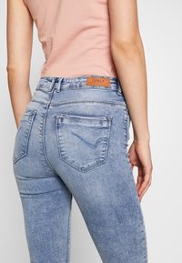 Vaqueros de cintura alta de color azul claro con un lavado desgastado, diseño de cinco bolsillos y una etiqueta de cuero marrón en la parte trasera de la cinturilla.