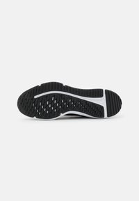 Semelle de chaussure de sport noire avec une surface en caoutchouc texturée et un motif en zigzag, entourée d'un bord blanc. Conception durable et flexible.