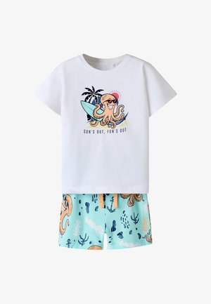 Weißes T-Shirt mit einem Oktopus, der eine Sonnenbrille trägt und ein Surfbrett hält, kombiniert mit blauen Shorts mit meeresthematischen Mustern und Oktopussen.