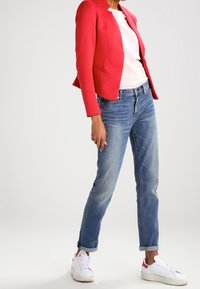 Rød tekstureret blazer, hvid og lyserød stribet t-shirt, blå slim-fit jeans og hvide sneakers med røde detaljer.