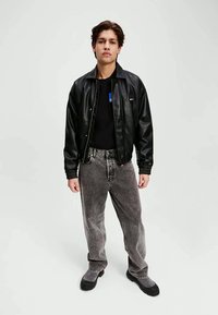 Svart skinn bomberjakke over en svart t-skjorte, sammen med grå denimjeans. Skoene inkluderer svarte ankelstøvler. En enkel og uformell stil.
