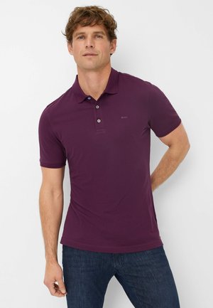 Brax lila Poloshirt mit kurzen Ärmeln, dreiknöpfigem Kragen und dezentem Logo-Detail. Kombiniert mit dunkelblauen Jeans, die eine glatte Textur aufweisen.