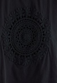 Sort stof med et hævet, cirkulært hæklemønster, der indeholder koncentriske ringe og blomsterlignende former langs kanterne.