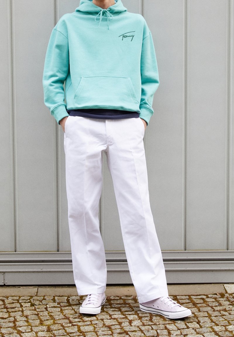 Sudadera verde menta con un bolsillo frontal y logo, combinada con pantalones anchos blancos y zapatillas blancas. Tejido texturizado, diseño casual.