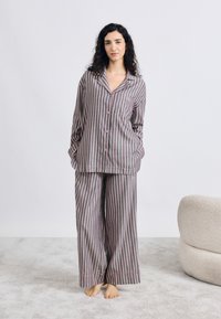 Conjunto de pijama a rayas con camisa de manga larga abotonada y pantalones de pierna ancha, en tonos gris y rosa. Tela suave, ajuste relajado.