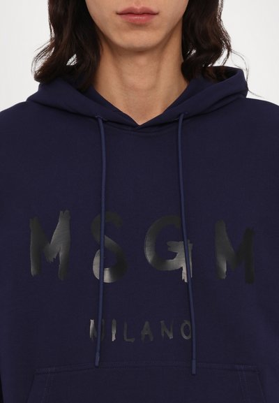 Felpa blu navy con cappuccio e lacci, caratterizzata da grandi lettere nere, consumate, stampate sul davanti con la dicitura "MSG" e "MILANO". Tessuto morbido.