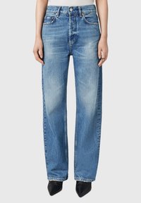 Jeans wide-leg in denim blu chiaro con vita alta, dotati di tasche frontali, passanti per cintura e un lavaggio sbiadito; abbinati a scarpe nere a punta.