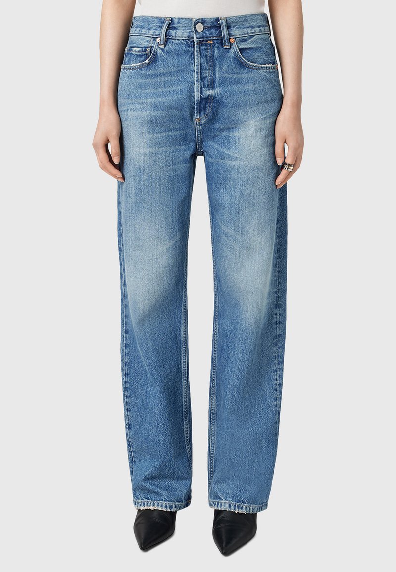 Jeans wide-leg in denim blu chiaro con vita alta, dotati di tasche frontali, passanti per cintura e un lavaggio sbiadito; abbinati a scarpe nere a punta.