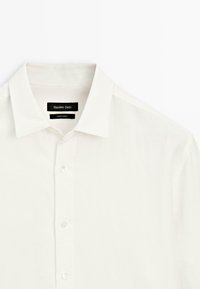 Weißes Leinenhemd mit klassischem Kragen, Knopfleiste vorne und einem kleinen Etikett, das "Massimo Dutti" und "Made in Turkey" anzeigt.