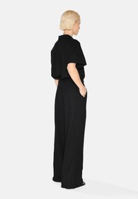 Chemise noire à manches courtes avec une coupe décontractée, associée à un pantalon large noir taille haute. Tissu lisse, design minimaliste, sans motifs visibles.