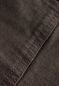 Detail tmavohnedého textilu zobrazujúci diagonálnu väzbu a vertikálny šitý šev.