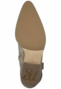 Suola della scarpa beige con una forma appuntita. Presenta una parte superiore texturizzata e decorata. Marchio impresso sul tallone e suola in gomma liscia.