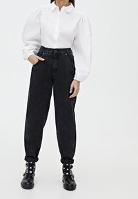 Camisa blanca de botones con mangas abullonadas, combinada con jeans de mezclilla negros de tiro alto. Botas militares negras con tachuelas plateadas.