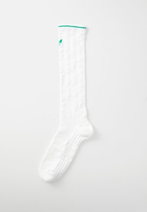 Biała skarpetka do kolan z prążkowaną teksturą, zielonym akcentem na górze i wyściełanym wnętrzem. Materiał wydaje się miękki i elastyczny.