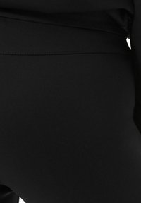 Czarne sportowe legginsy wykonane z gładkiego, elastycznego materiału, z bezszwowym pasem w talii i minimalnym zdobieniem.