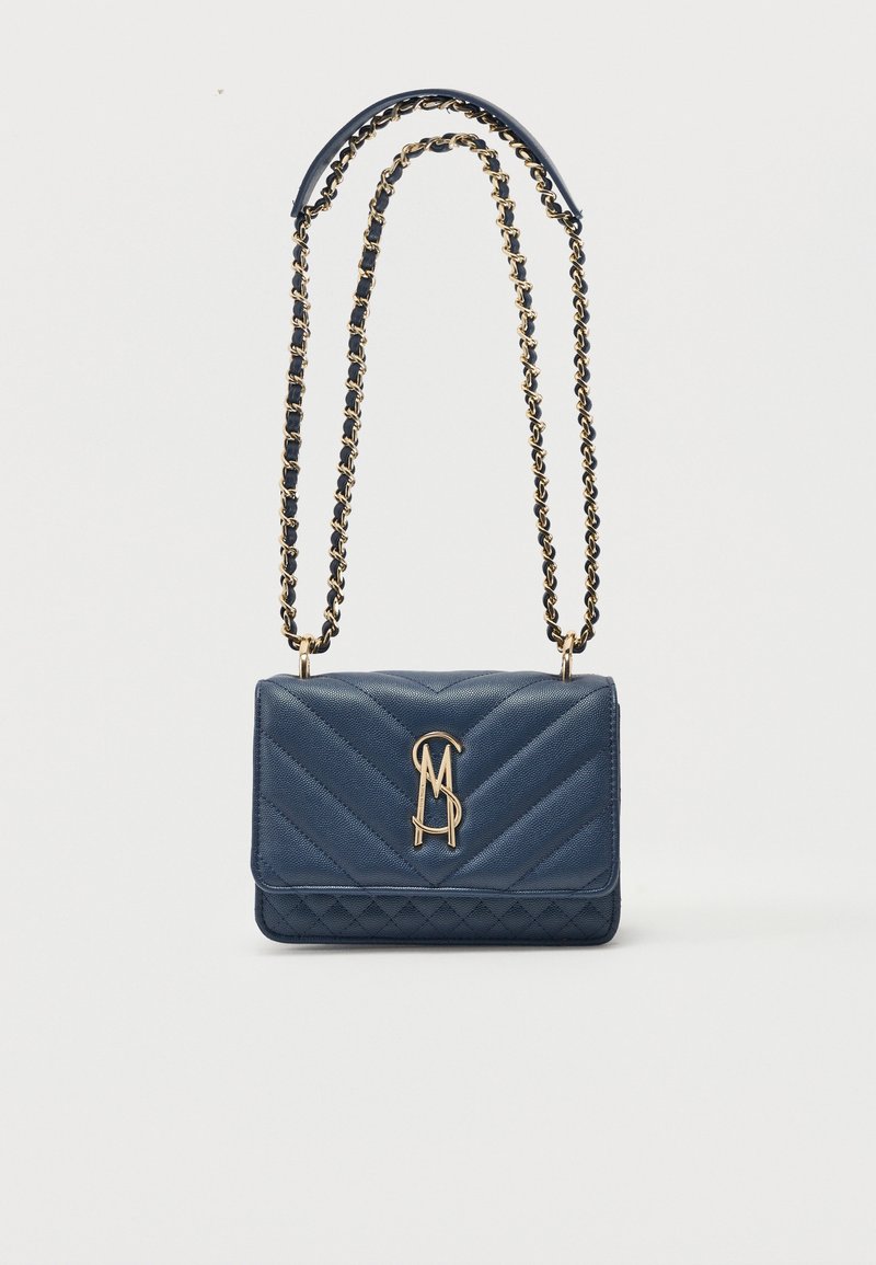 Τσάντα χειρός από δερμάτινο καπιτονέ σε ναυτικό μπλε με χρυσή αλυσίδα και χρυστό λογότυπο "MS" που συνδέεται μπροστά στο κλείσιμο του καπακιού.