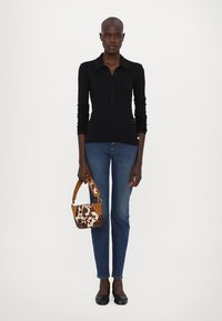 Svart ribbestrikket langermet topp med polo-krage, kombinert med blå rette jeans. Accessorisert med en liten, flerfarget håndveske.