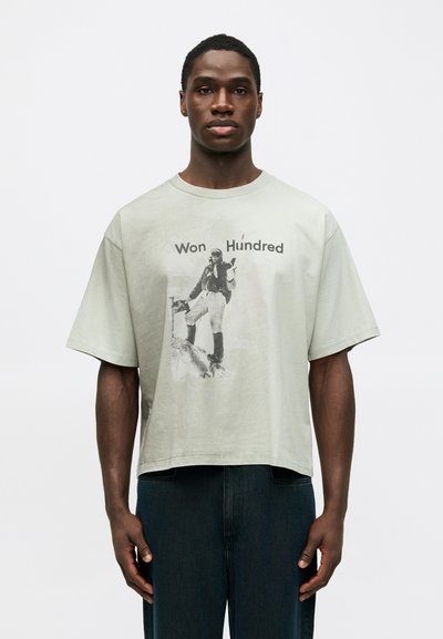 Lys grøn bomulds t-shirt med en boxy pasform, rund halsudskæring og trykt grafik af en figur. Bærer kontrasterende sorte jeans.