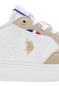 Sneaker bianco in pelle con dettagli dorati, finiture perforate e logo. Presenta strisce blu e rosse sulla linguetta. Suola piatta bianca.