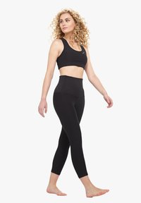 Fekete sportmelltartó és magas derekú leggings rugalmas anyagból. A leggings zökkenőmentes dizájnnal és testhez álló szabással rendelkezik.