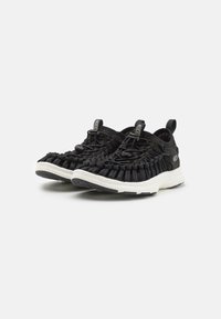 Sneaker nere intrecciate con tomaia testurizzata, lacci elastici e suola in gomma bianca. Presenta una linguetta sul tallone per facilitarne l'indossamento.