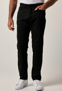 Pantalones de algodón negros con un corte ajustado, que cuentan con bolsillos frontales, pasadores para cinturón y un cierre clásico de botón, combinados con zapatillas blancas.