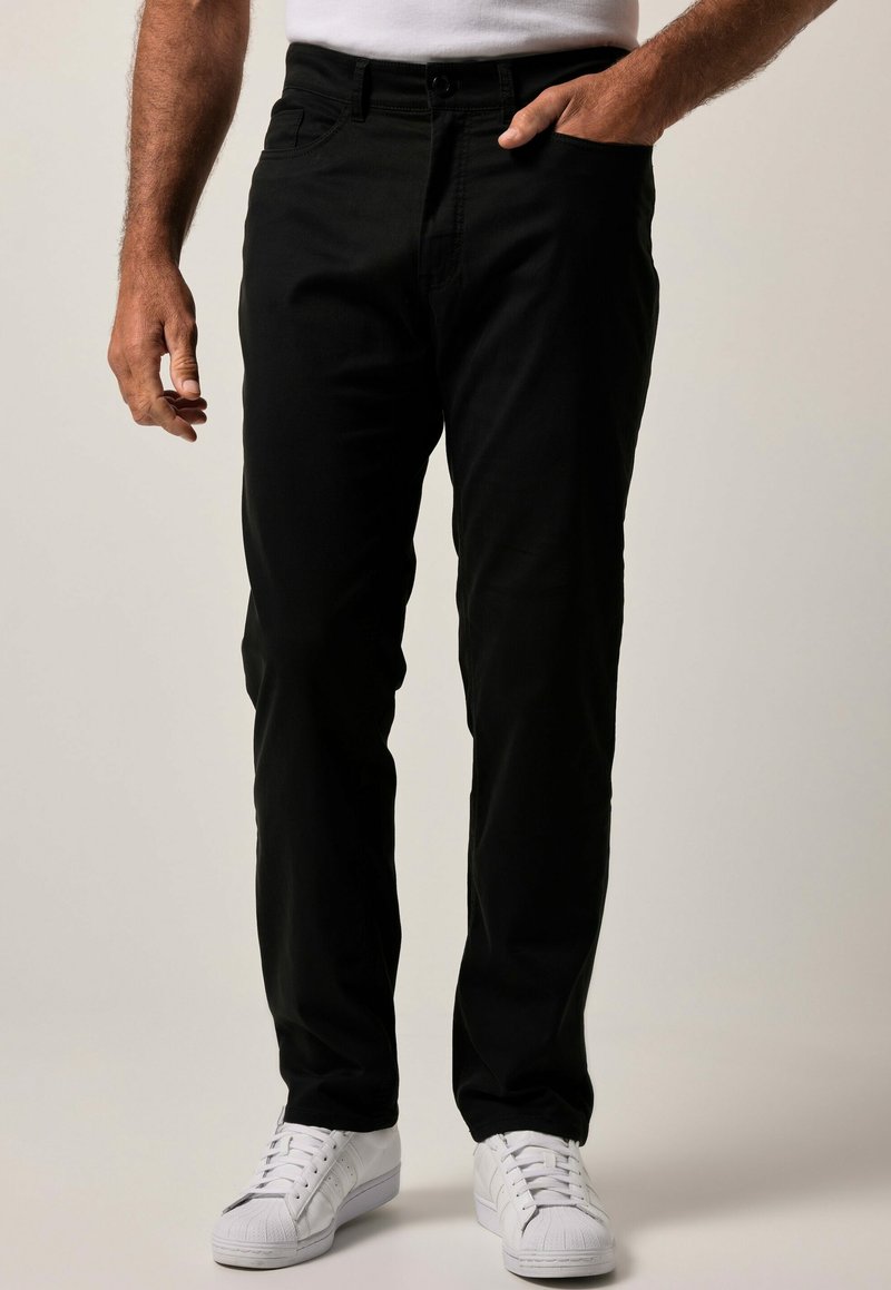 Pantalones de algodón negros con un corte ajustado, que cuentan con bolsillos frontales, pasadores para cinturón y un cierre clásico de botón, combinados con zapatillas blancas.