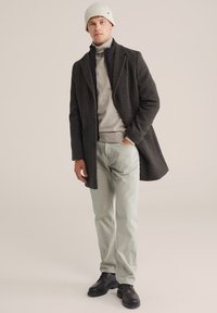 Pelēks vilnas mētelis virs gaiši pelēka turtlenecka, apvienots ar gaiši zaļām biksēm un melniem kurpju šņorējamiem apaviem. Aksesuāri - balta adīta cepure.