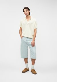 Λαμπερό κρεμ κοντομάνικο πόλο με κάθετες ρίγες; ανοιχτό μπλε κοντομάνικο τζιν σορτσάκι; καφέ σουέτ παπούτσια; λευκές κάλτσες μέχρι τον αστράγαλο.