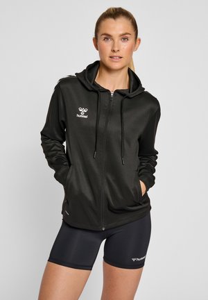 Svart zip-up hoodie med framficka och dragsko på huvan. Har en vit logotyp på vänster bröst och en slät, något glänsande tyg.