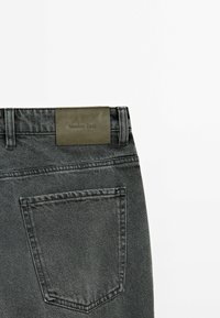 Gray denim jeans with a textured surface, featuring a leather label with "Massimo Dutti," and a single rear pocket.
