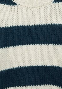 Pletená látka svetru s vodorovnými pruhy v tmavě modré a krémové barvě. Textura je měkká s robustním pleteným vzorem.