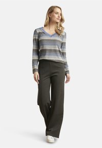 V-neck sweater with blue and gray zigzag pattern, paired with high-waisted dark gray wide-leg trousers and white sneakers.