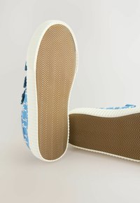 Baskets bleues à motifs avec semelles blanches, dotées d'une semelle en chevron texturée. Bandes auto-agrippantes sur le côté pour un ajustement facile.