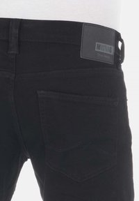 Los pantalones vaqueros de denim negro tienen un corte slim con un diseño clásico. Incluyen una etiqueta de cuero en la cinturilla y un patrón de costura distintivo en el bolsillo trasero.