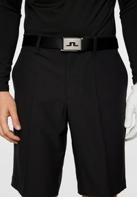 Czarne szorty o gładkiej teksturze, z eleganckim krojem, przednimi fałdami oraz błyszcząca metalową klamrą z logo.